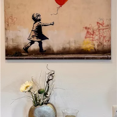 Ein Mädchen, das einen roten Herzballon in der Hand hält, steht vor einer grauen Wand mit Graffiti. Die Atmosphäre wirkt nostalgisch und gefühlvoll.