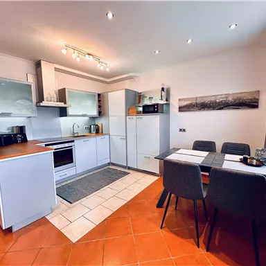 Moderne Küche mit hellen Möbeln und einem Esstisch. Der Raum ist gut beleuchtet und hat eine einladende Atmosphäre.