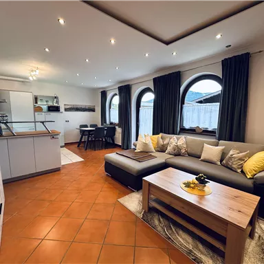 Ein modernes Wohnzimmer mit einer gemütlichen Couch und einem Holztisch. Die großen Fenster sorgen für viel Tageslicht und eine einladende Atmosphäre.