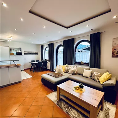 Ein modernes Wohnzimmer mit einem bequemen Sofa und einem Holzkaffee-Tisch. Große Fenster und stilvolle Dekoration sorgen für eine einladende Atmosphäre.