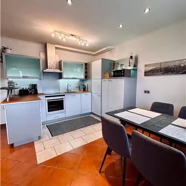 Eine moderne Küche mit weißen Schränken und einem eleganten Esstisch. Der Raum ist hell und freundlich gestaltet.