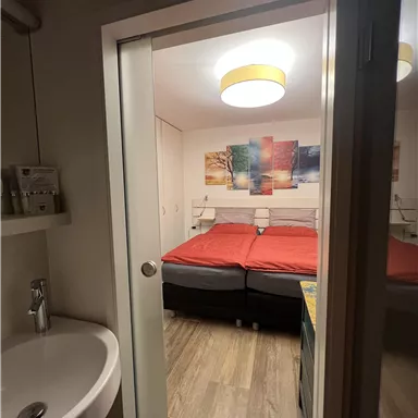 A cozy bedroom with two red beds and a modern ceiling light. In the foreground, a sink is visible.