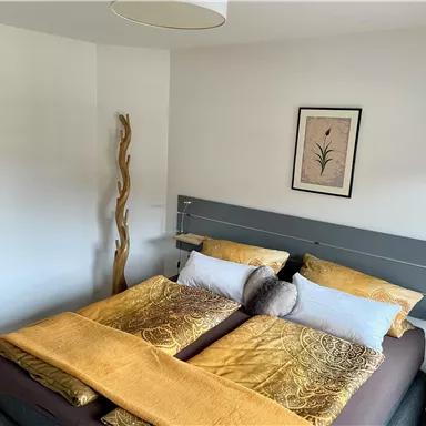 A cozy bedroom with a large double bed and yellow bedspreads. A decorative picture hangs on the wall, and a wooden sculpture stands in the room.