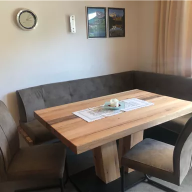 Ein gemütlicher Essbereich mit einem Holztisch und einer U-förmigen Bank. Zwei Stühle ergänzen den Raum, der eine helle und einladende Atmosphäre hat.