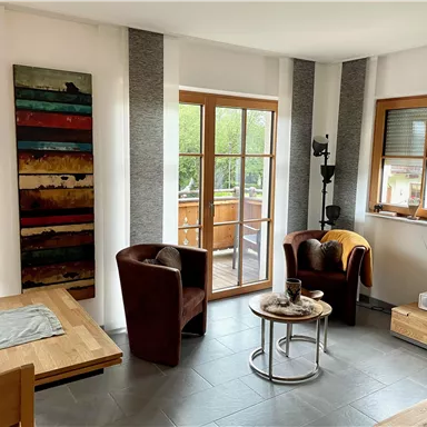 A modern living room with two cozy armchairs and a table. Large windows let in plenty of light and provide a view of the outdoor area.