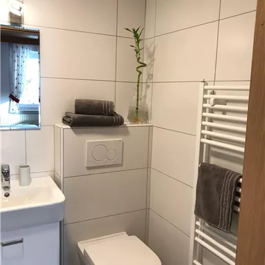 Ein modernes Badezimmer mit heller Fliesenwand. Es enthält ein Waschbecken, eine Toilette und Handtücher auf einem Handtuchhalter.