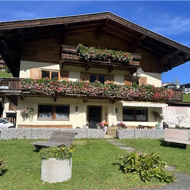 A charming alpine house with blooming flowers on the balcony. The surroundings are green and inviting, perfect for a relaxing stay.