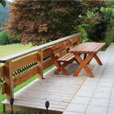 Ein gemütlicher Terrassenbereich mit einem Holztisch und Bänken. Im Hintergrund sind grüne Felder und Bäume zu sehen.