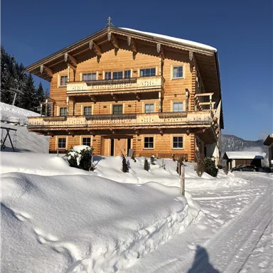 A cozy wooden house in winter, surrounded by snowy landscapes. The clear sky and the snow give the scene a calm atmosphere.