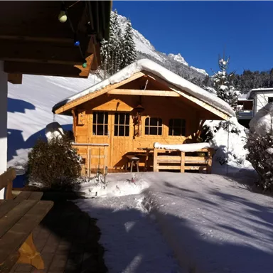 Ein gemütliches Holzhaus im Schnee vor einem klaren blauen Himmel. Die Umgebung ist winterlich und friedlich.