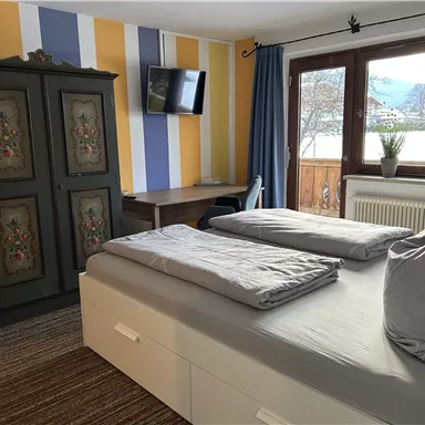 A cozy bedroom with a large bed and a beautiful dresser. The room has colorful walls and a window with a view of the mountains.