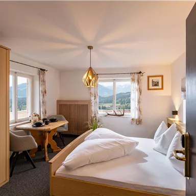 Ein gemütliches Schlafzimmer mit einem großen Fenster, das einen Blick auf die Landschaft bietet. Der Raum ist modern eingerichtet mit einem Doppelbett, einem Tisch und Stühlen.