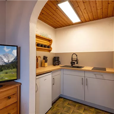 Eine moderne Küche mit Holzregalen und einem Fernseher. Der Raum hat eine helle Atmosphäre und eine panoramische Aussicht auf die Berge.