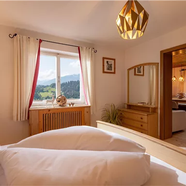 Ein gemütliches Schlafzimmer mit zwei Betten und einem großen Fenster, das einen Blick auf die Berge bietet. Das Interieur ist warm und einladend mit einem Holzschrank und dekorativen Elementen.