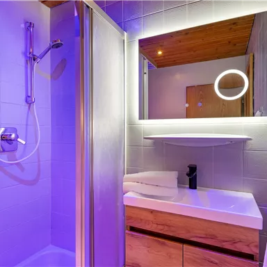 Ein modernes Badezimmer mit einer Dusche und einem großen Spiegel. Die Beleuchtung erzeugt eine angenehme Atmosphäre mit sanften Farben.