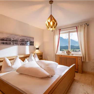 Ein gemütliches Schlafzimmer mit einem Doppelbett und weißen Kissen. Große Fenster bieten einen schönen Blick auf die Berge.