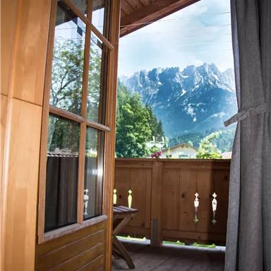 Ein Blick von einem Balkon auf majestätische Berge. Der Raum ist von warmem Holz umgeben und hat einen gemütlichen Charme.