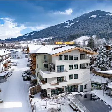 A winter view of the hotel with snow-covered roofs and surrounding mountains. The landscape is peaceful and inviting.