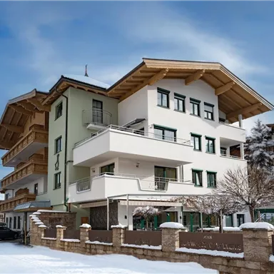A modern building in alpine style, surrounded by snow and a clear sky. In the foreground, a quiet road with some vehicles can be seen.