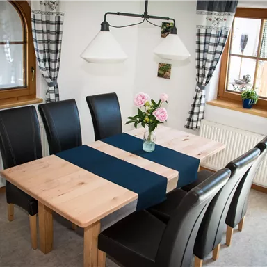 Ein gemütlicher Essbereich mit einem Holz-Esstisch und schwarzen Stühlen. Auf dem Tisch steht eine Blumenvase mit Rosen.