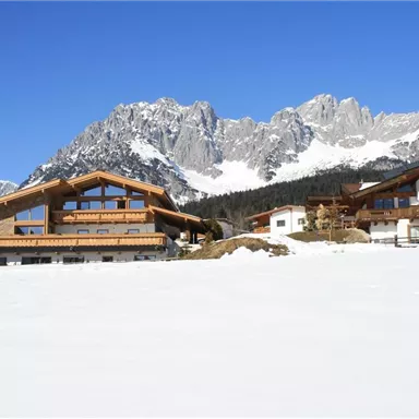 An impressive mountain landscape with snow-covered meadows and majestic peaks. In the foreground, there are modern chalets that are harmoniously integrated into the surroundings.