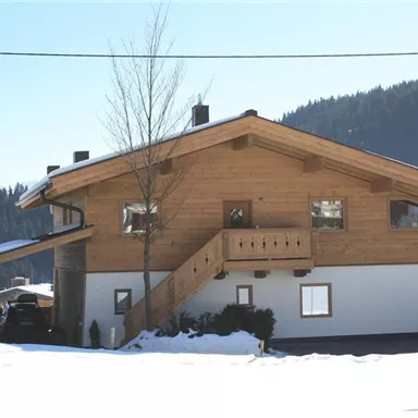 Ein gemütliches Chalet im Winter, umgeben von Schnee und Bergen. Die Holz-Architektur verleiht dem Haus einen rustikalen Charme.