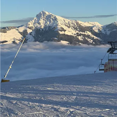 A beautiful snowy landscape with a majestic mountain in the background. The scene features a ski slope and a ski lift above the fog.