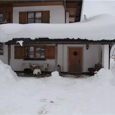 Eine verschneite Fassade eines Hauses mit dicken Schneeverwehungen. Der Eingang ist gut sichtbar, jedoch von Schnee umgeben.