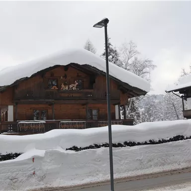 Ein traditionelles Holzhaus mit einem schneebedeckten Dach. Umgeben von Winterlandschaft und frischem Schnee.