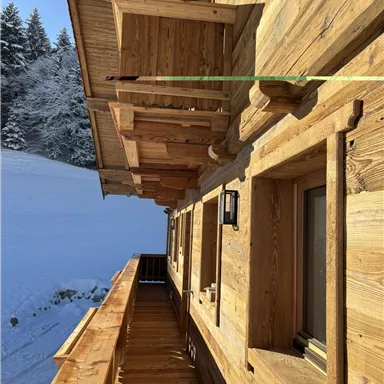 A wooden house with a balcony, surrounded by snow-covered landscapes. The architecture is traditional and cozy.