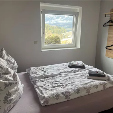 Ein gemütliches Schlafzimmer mit zwei Betten und Blumenmuster. Ein Fenster bietet einen Blick auf die Berge und die Natur draußen.