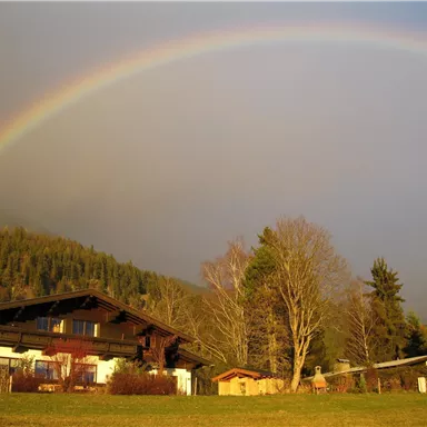 A picturesque house with a rainbow in the background. The surroundings are characterized by trees and green meadows.