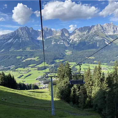 A picturesque mountain landscape with green meadows and tall mountains in the background. A cable car travels through the beautiful nature.