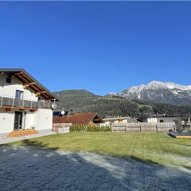 Ein modernes Haus mit einem großen Garten und Blick auf die Berge. Der Himmel ist klar und blau.