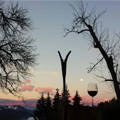 A picturesque landscape with bare trees, a glass of wine, and a gentle sunset. The sky is tinted in soft shades of pink and blue.