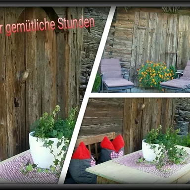 Eine gemütliche Terrasse mit zwei Liegen, dekoriert mit bunten Blumen und Kräutertöpfen. Der rustikale Holzbau schafft eine einladende Atmosphäre.