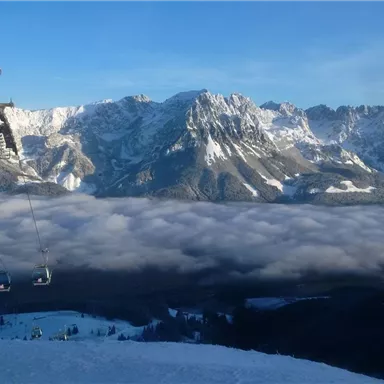 Eine Winterlandschaft mit schneebedeckten Bergen und einer Seilbahn. Im Hintergrund liegt eine Wolkendecke.