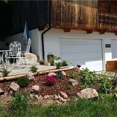 A beautiful outdoor area with a small garden and seating furniture. The garages are visible in the background, surrounded by a green landscape.