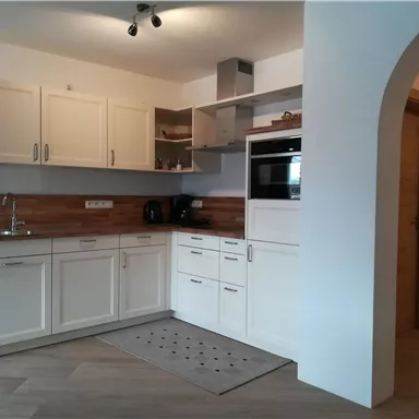 A modern kitchen with white cabinets and wooden details. It is well-equipped and has plenty of natural light.