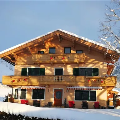 Ein traditionelles alpenländisches Haus, umgeben von Schnee und Bergen. Die Fassade hat charmante Balkone und Fenster mit geschmückten Fensterläden.