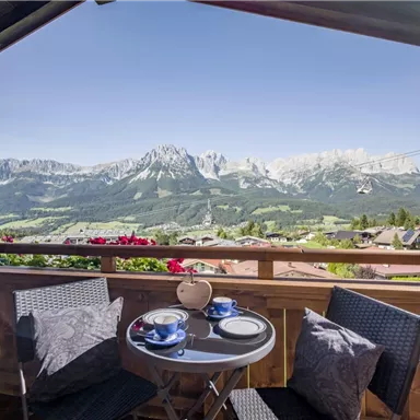 Ein gemütlicher Balkon mit einem Tisch und Stühlen, der einen herrlichen Blick auf die Berge bietet. Die Landschaft ist grün und die Berge sind mit Schnee bedeckt.