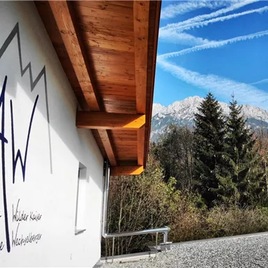 A view of the mountain landscape with a clear blue sky. The inscription "AW Apartments Familie Keller" is visible on the wall of the building.