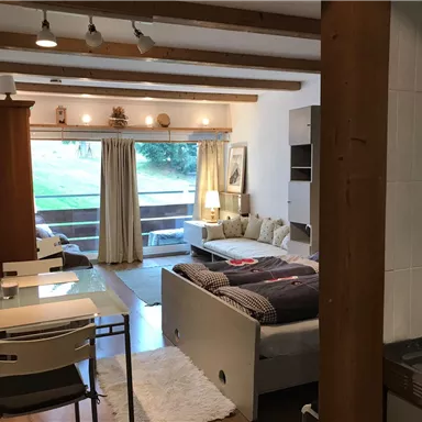 A cozy room with a double bed, a sofa, and a large window. The room features wooden details and a small dining table.