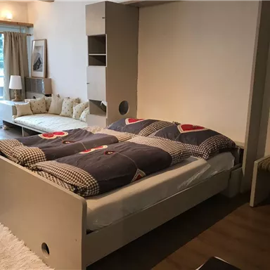 A cozy bedroom with a bed and a modern seating area. Large windows let in plenty of light and provide a view of nature.