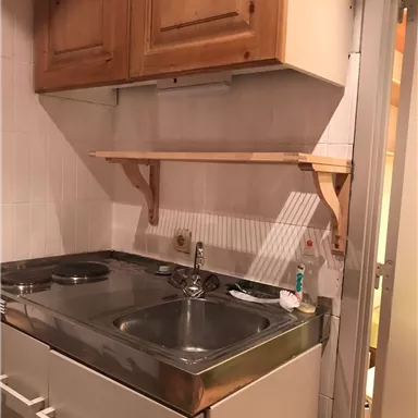 A small kitchenette with a double sink and two hot plates. Above the countertop, there is a wooden shelf.
