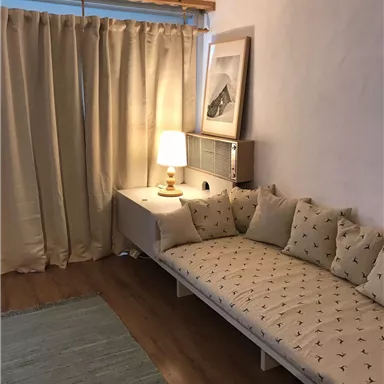 A cozy living space with a padded sofa and a floor lamp. Curtains and a carpet enhance the inviting atmosphere.