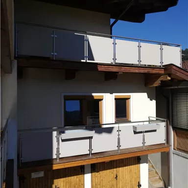 A modern building with two floors and balconies. The facade combines wood and plaster, and the sky is clear.
