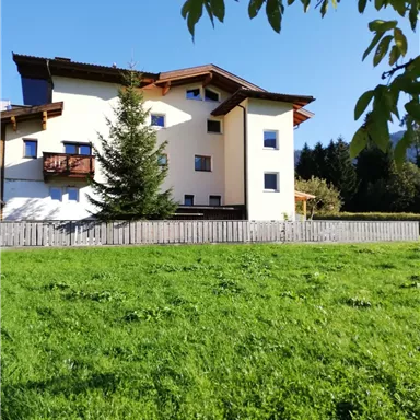A modern house with a bright exterior paint and wooden elements. Surrounded by a green lawn and trees, it is located in a quiet environment.