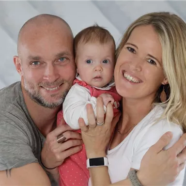 A happy family with a baby. The father and mother are hugging their child and smiling.