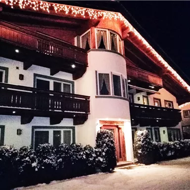 A cozy chalet with Christmas lights at night. The snow surrounds the building and creates a festive atmosphere.